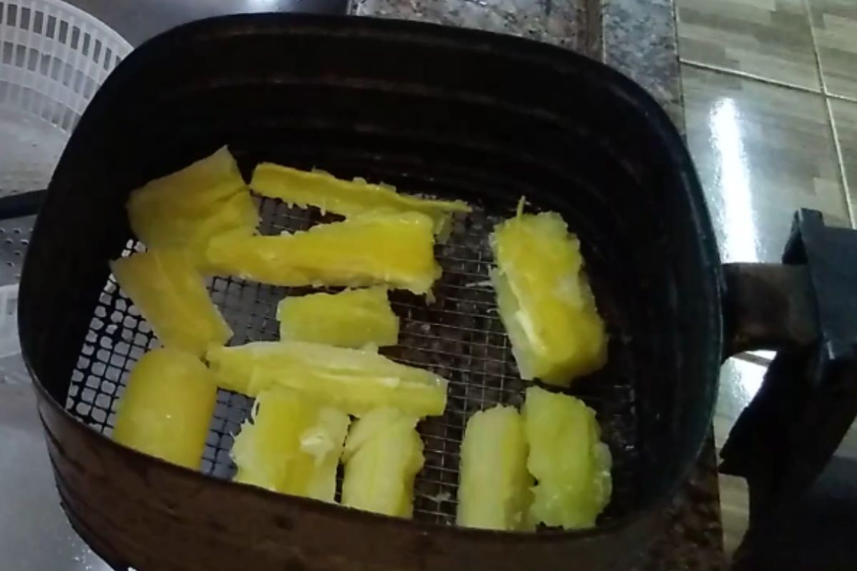 Pedaços de mandioca cozida distribuídos na cesta da airfryer antes do preparo