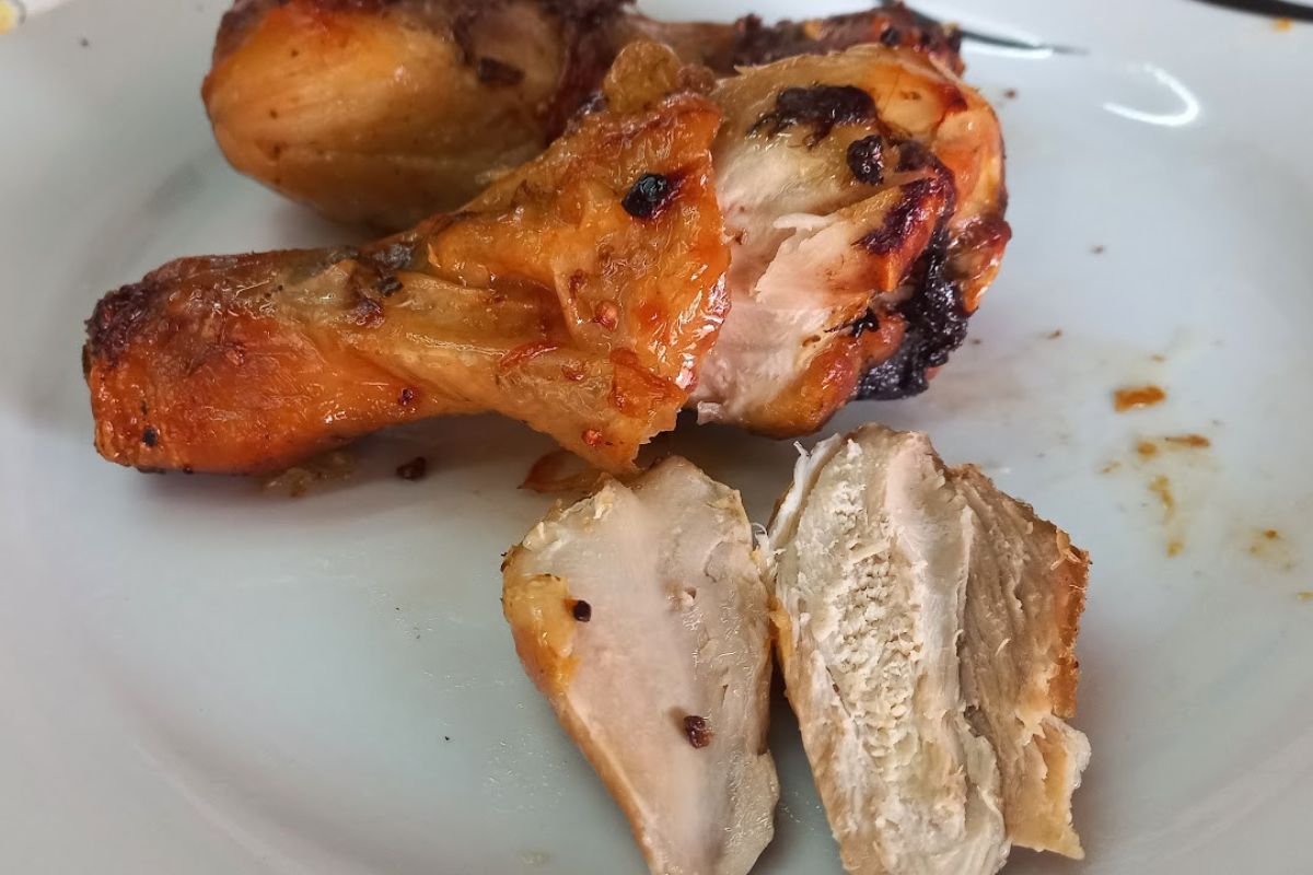 Close-up de coxas de frango assadas em um prato branco, com uma peça cortada ao meio revelando a carne interna suculenta e bem cozida