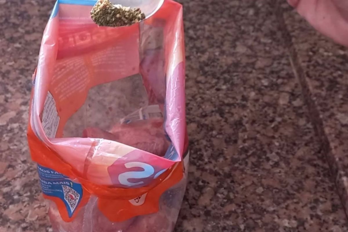 Uma colher despejando tempero de ervas secas dentro de um saco plástico com coxas de frango cruas sobre uma bancada de granito