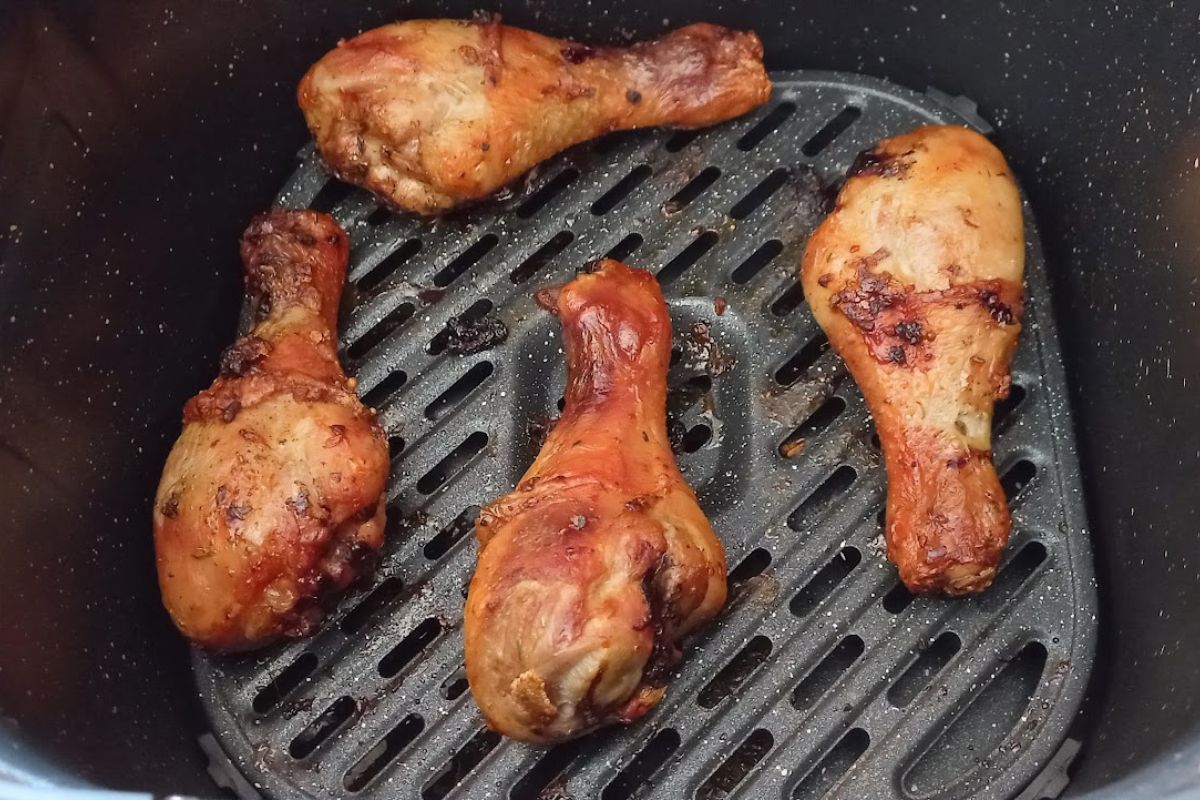 Quatro coxas de frango assadas na airfryer com a pele bem dourada e crocante dispostas sobre a grade interna do cesto