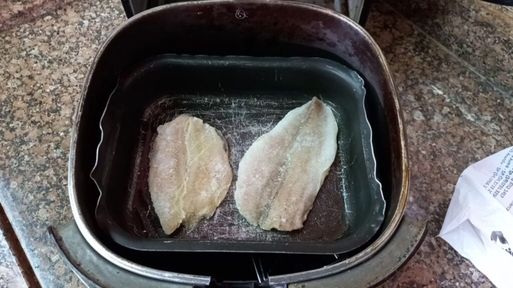 Filé de merluza cru disposto na airfryer antes do preparo