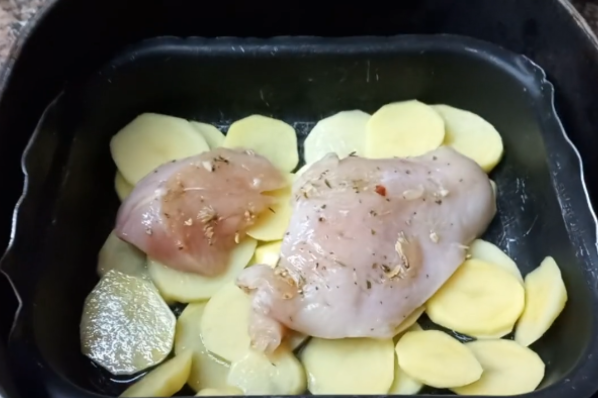 Peito de frango cru temperado sobre rodelas de batata dentro da cesta da airfryer, antes do preparo