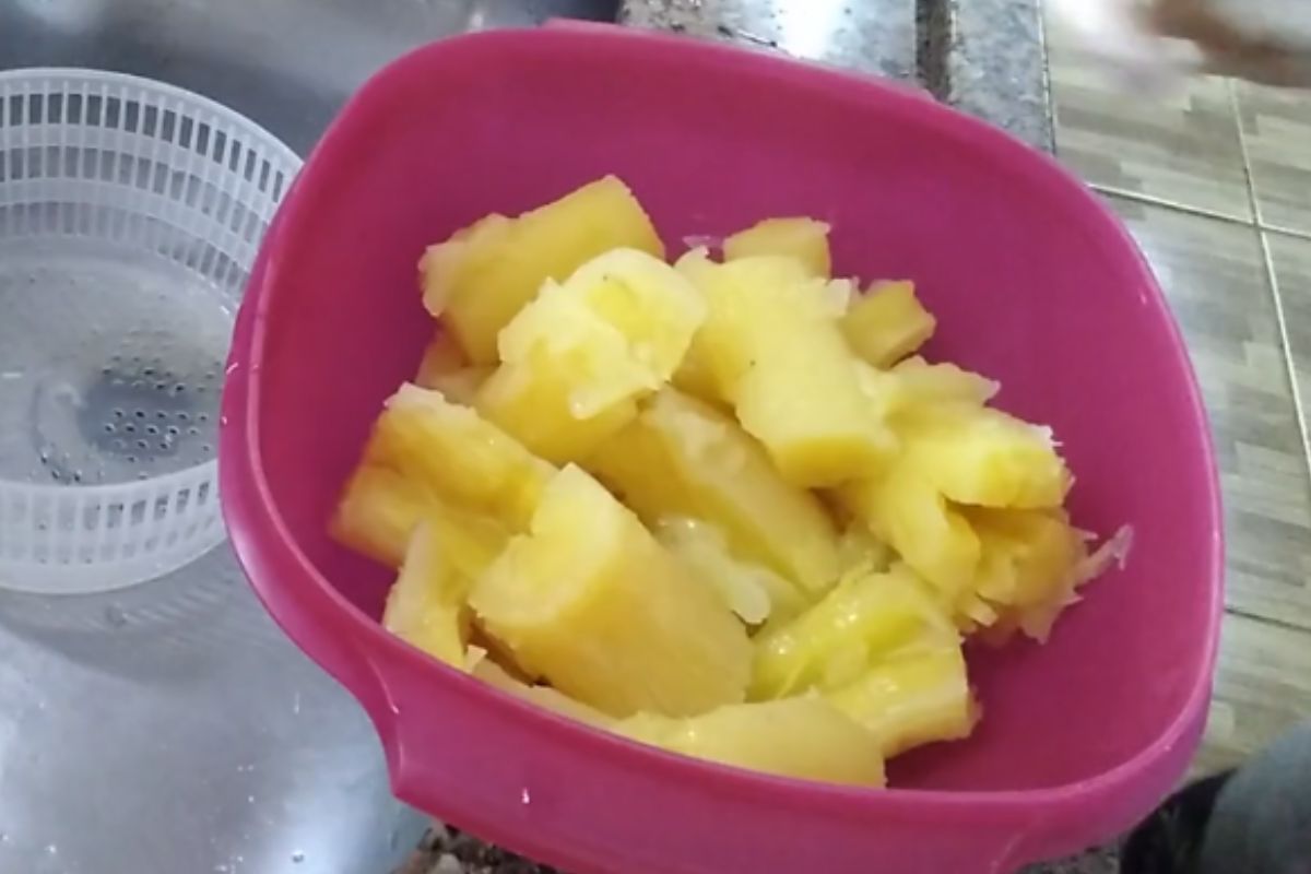 Mandioca cozida em pedaços escorrendo água, colocada em recipiente antes de ir para a airfryer