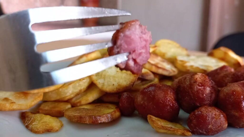 Pedaço de linguiça sendo servido no garfo após preparo na airfryer
