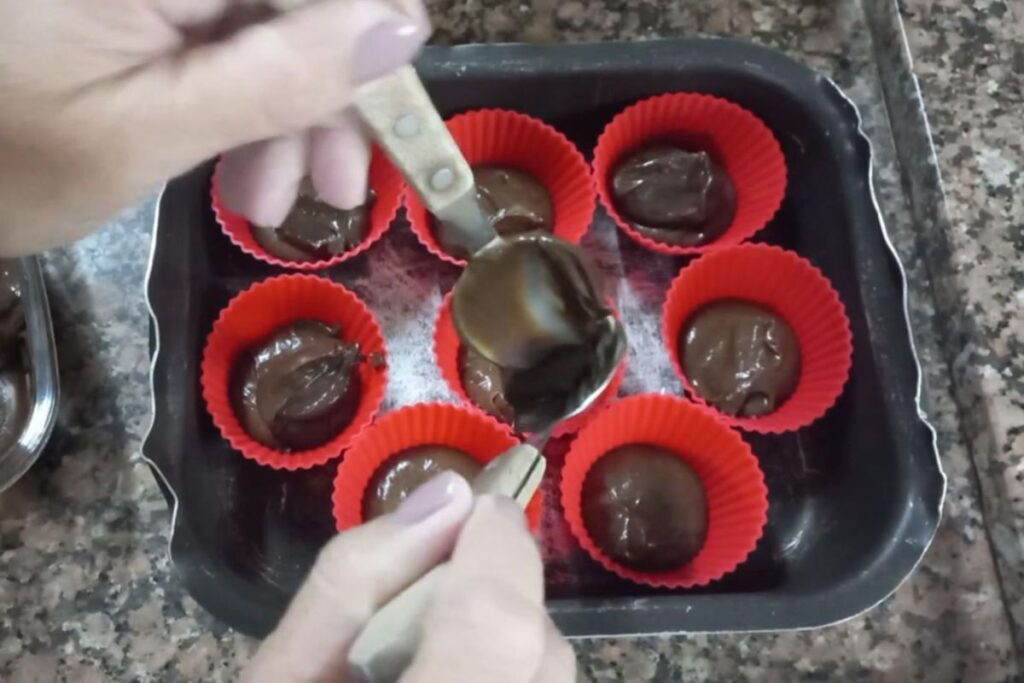 Massa de chocolate sendo colocada em forminhas de silicone coloridas para cupcake