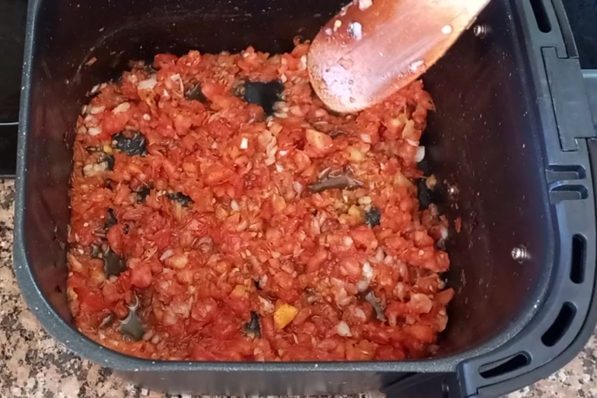 Molho de tomate caseiro em preparo na cesta da airfryer, com tomates e cebola refogados e sendo mexidos.